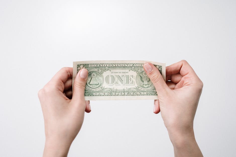 A close-up image of hands holding a one dollar bill, symbolizing finance and economy.